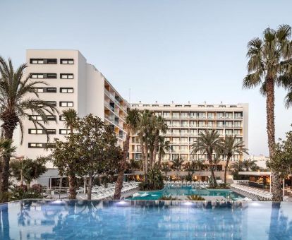 Moderno hotel solo para adultos con grandes piscinas al aire libre, solarium con tumbonas y palmeras.