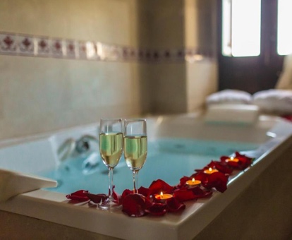 Foto de la bañera de hiromasaje con dos copas de champán, velas y pétalos de rosa decorativos