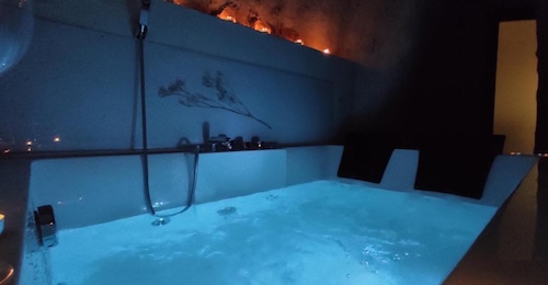 Foto del cuarto de baño con el jacuzzi bajo el techo de piedra, lleno de agua y con luces azules de cromoterapia