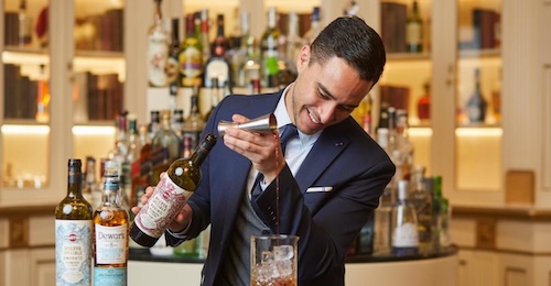 Un barman con una botellas al fondo preparando un cocktel en el bar de Hotel El Palace Barcelona