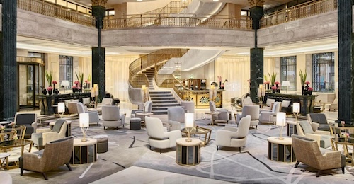 Foto del hall del Hotel Four Seasons de Madrid con mesas con decoración elegante y una escalera de caracol al fondo que lleva a la planta superior