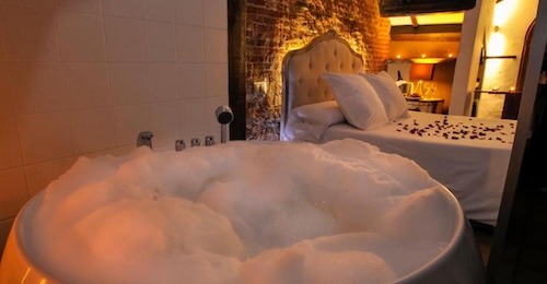 Foto de la bañera de hidromasaje junto a la cama cubierta de pétalos de rosas en el Hotel Rural con Jacuzzi La Viña