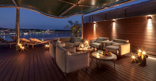 Foto de la terraza con mesas para tomar una copa rodeado de luces y con vistas al mar por la noche