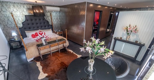 Cama llena de pétalos de rosas en una suite con una piel de vaca en el suelo y decoración moderna en el Nastasi Hotel & Spa