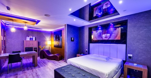 Foto de la cama debajo de un espejo en el techo y con un sillón tantra al fondo ideal para dar rienda suelta a la pasión de los clientes del Zouk Hotel
