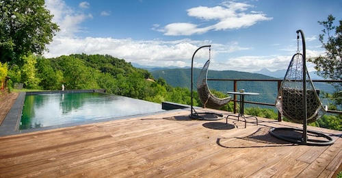 dos sillas colgantes sobre suelo de madera en el exterior junto a una piscina de borde infinito y con espectaculares vistas a la montaña y el campo